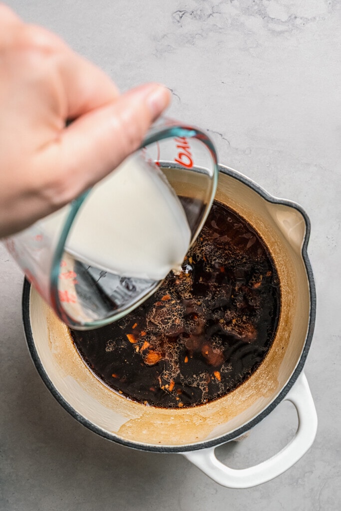 A cornstarch slurry is poured into a pot of teriyaki sauce.