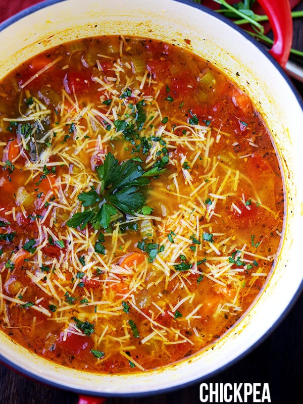 Overhead view of a pot of vegetable soup garnished with parsley and grated parmesan cheese.