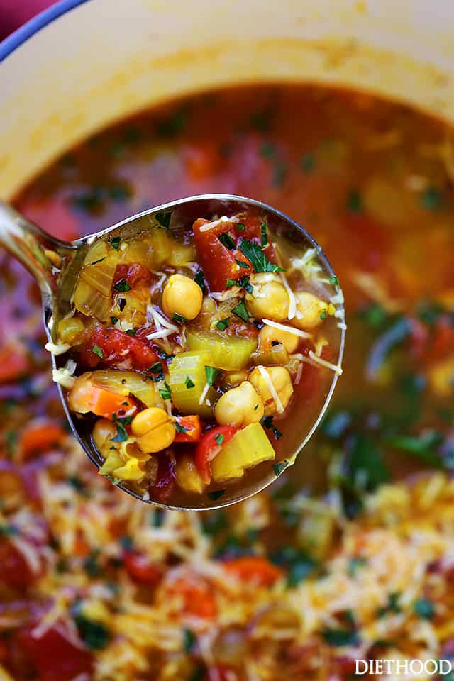 Overhead close up view of a ladle scooping vegetable soup from a large pot below.