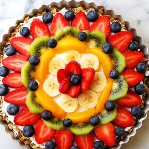 Overhead image of a fruit pizza topped with a blend of berries, bananas, peaches, and kiwi.