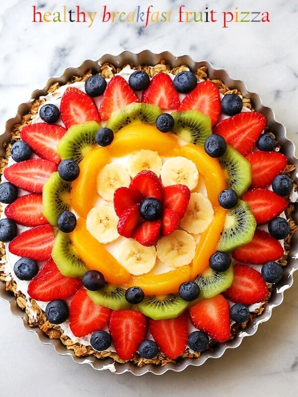 Overhead image of a fruit pizza topped with a blend of berries, bananas, peaches, and kiwi.
