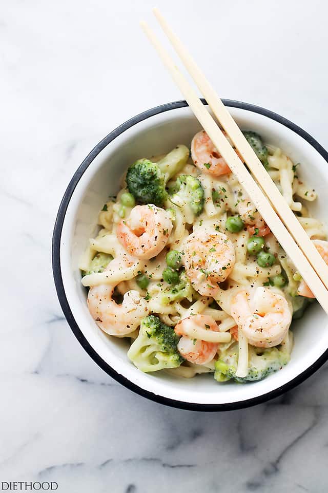 Overhead shot of a bowl of shrimp alfredo, with chopsticks resting on the rim of the bowl.