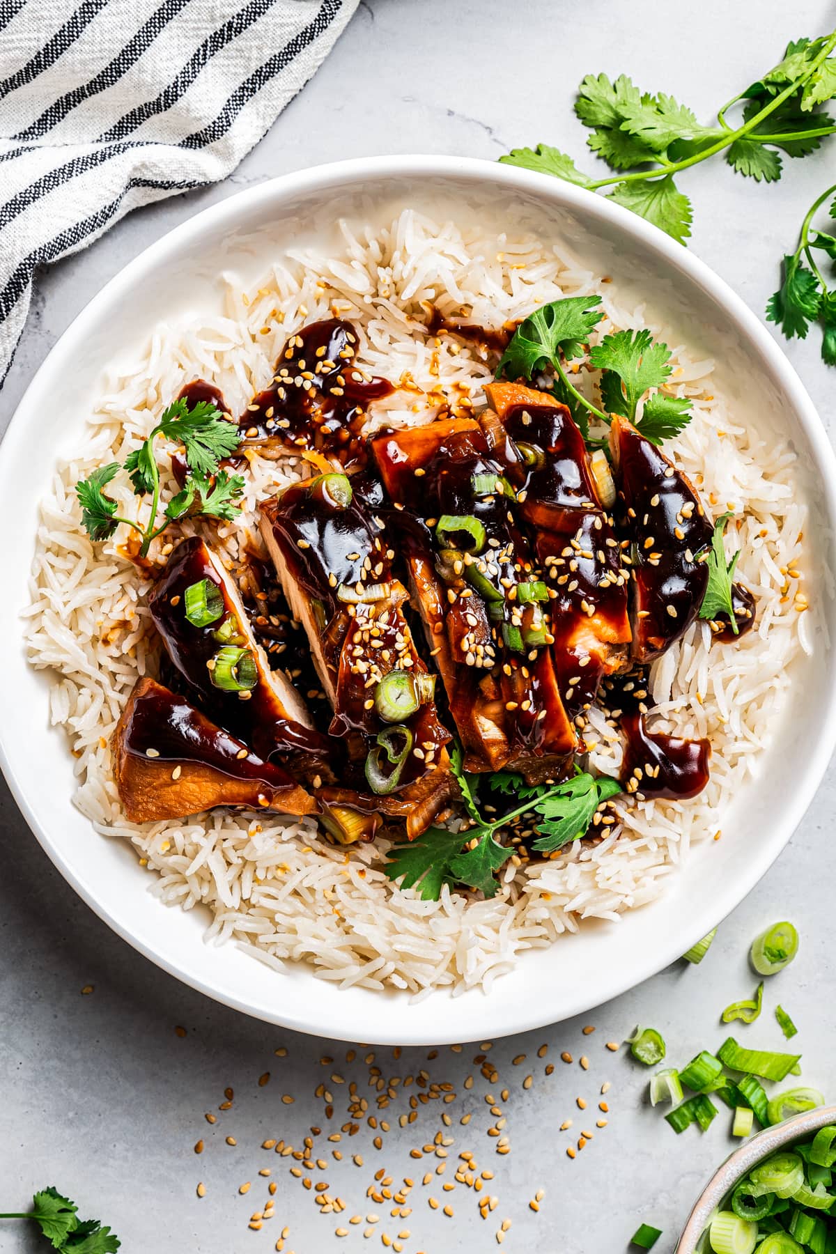 Chicken teriyaki served over rice on a white plate, garnished with green onions and sesame seeds, with a set of chopsticks.