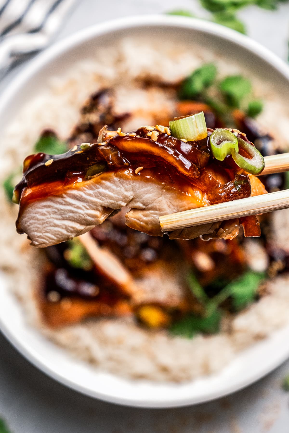 Close-up of a piece of chicken held above a plate of chicken served over rice.