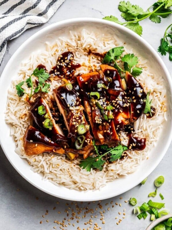 Chicken teriyaki served over rice on a white plate, garnished with green onions and sesame seeds, with a set of chopsticks.