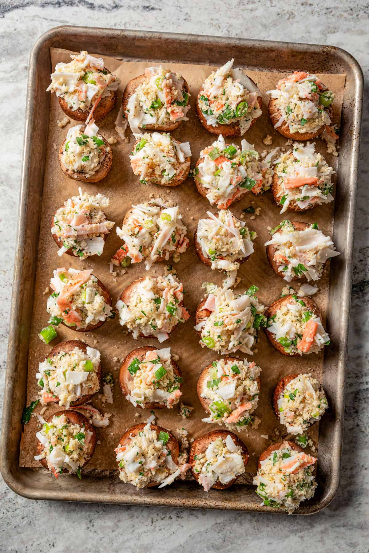 Overhead view of rows of crab stuffed mushrooms on a baking sheet.