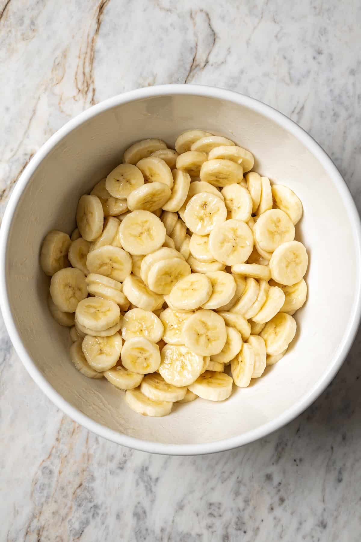 Banana slices tossed with lemon juice in a white bowl.