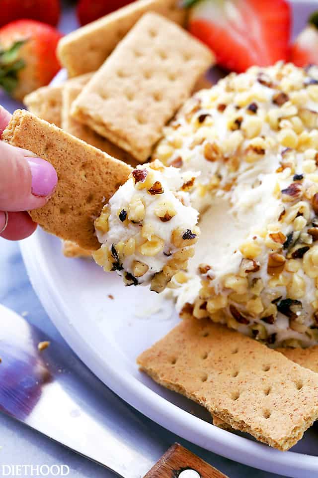 A graham cracker being dipped into a White Chocolate Cheeseball 