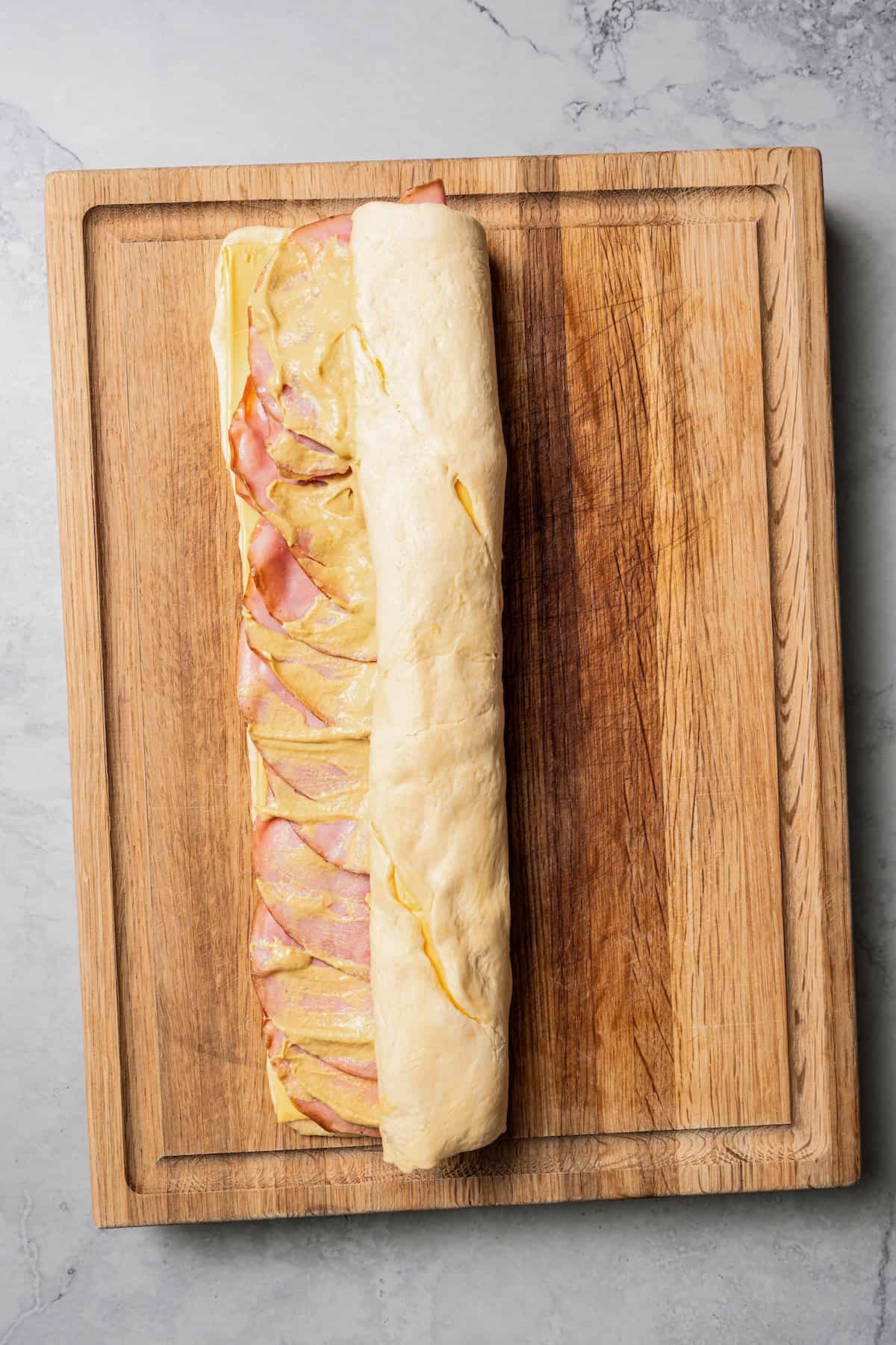 Crescent roll dough partially rolled up around the ham and cheese filling on a wooden cutting board.