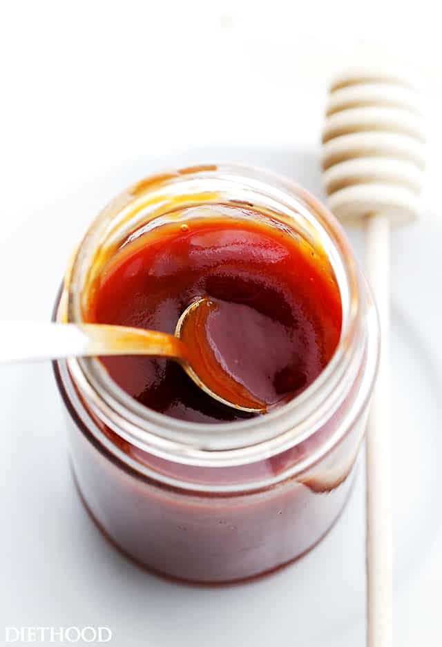 This slow-simmered honey barbecue sauce is a sweet and tangy homemade recipe that you can use on everything from chicken to ribs and chops! Overhead view of a spoon resting in an open jar of homemade honey barbecue sauce next to a honey dipper.