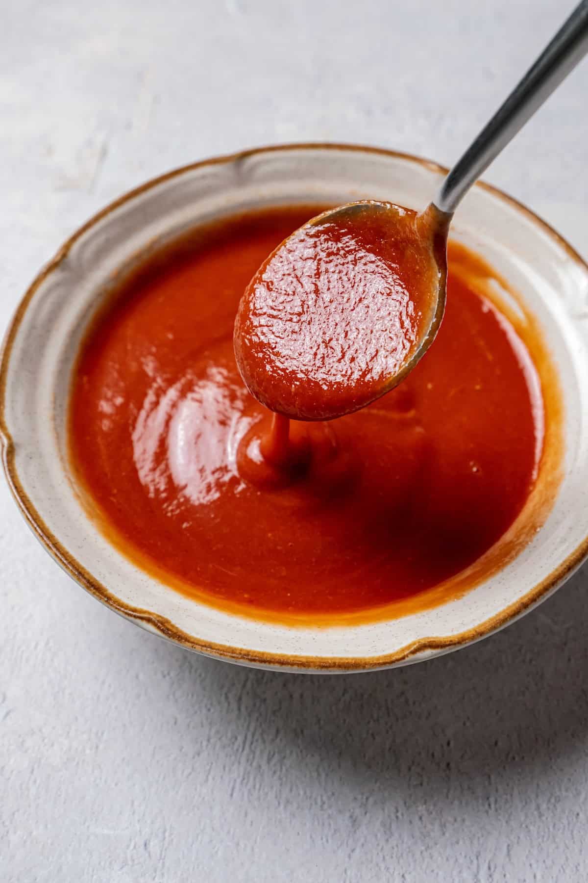 A spoon dripping meatloaf glaze into a stoneware bowl.