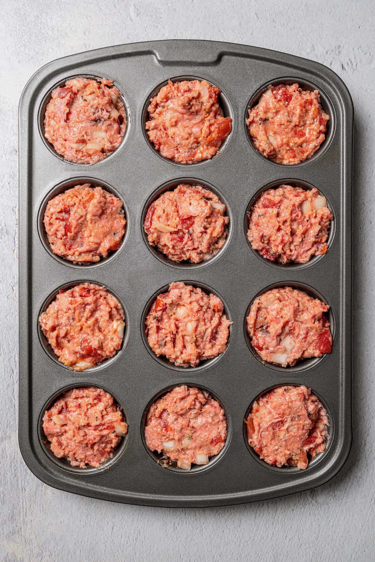 A 12-well muffin tin filled with turkey meatloaf mixture.