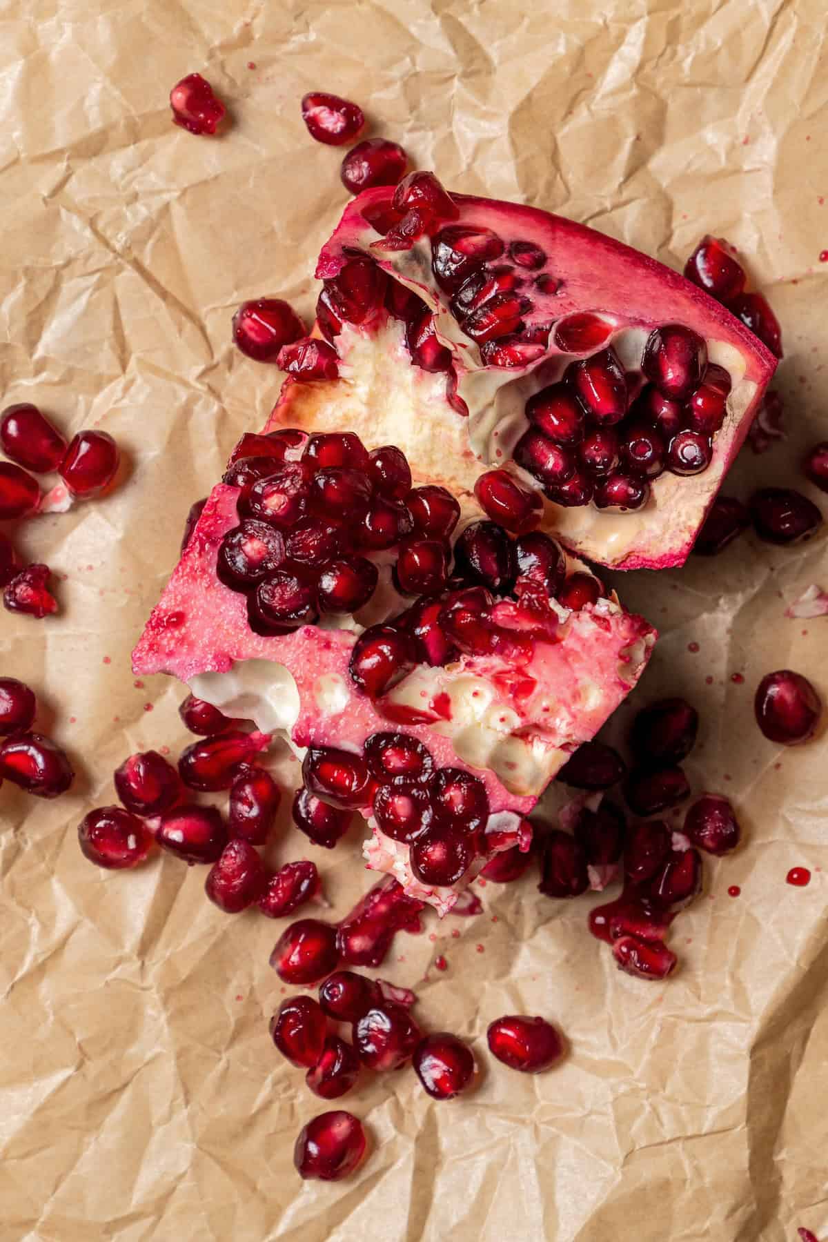 Close up of a partially deseeded pomegranate on a sheet of brown parchment paper.