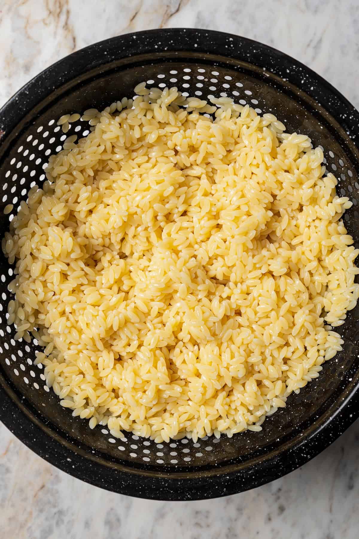 Cooked and drained orzo pasta in a black colander.