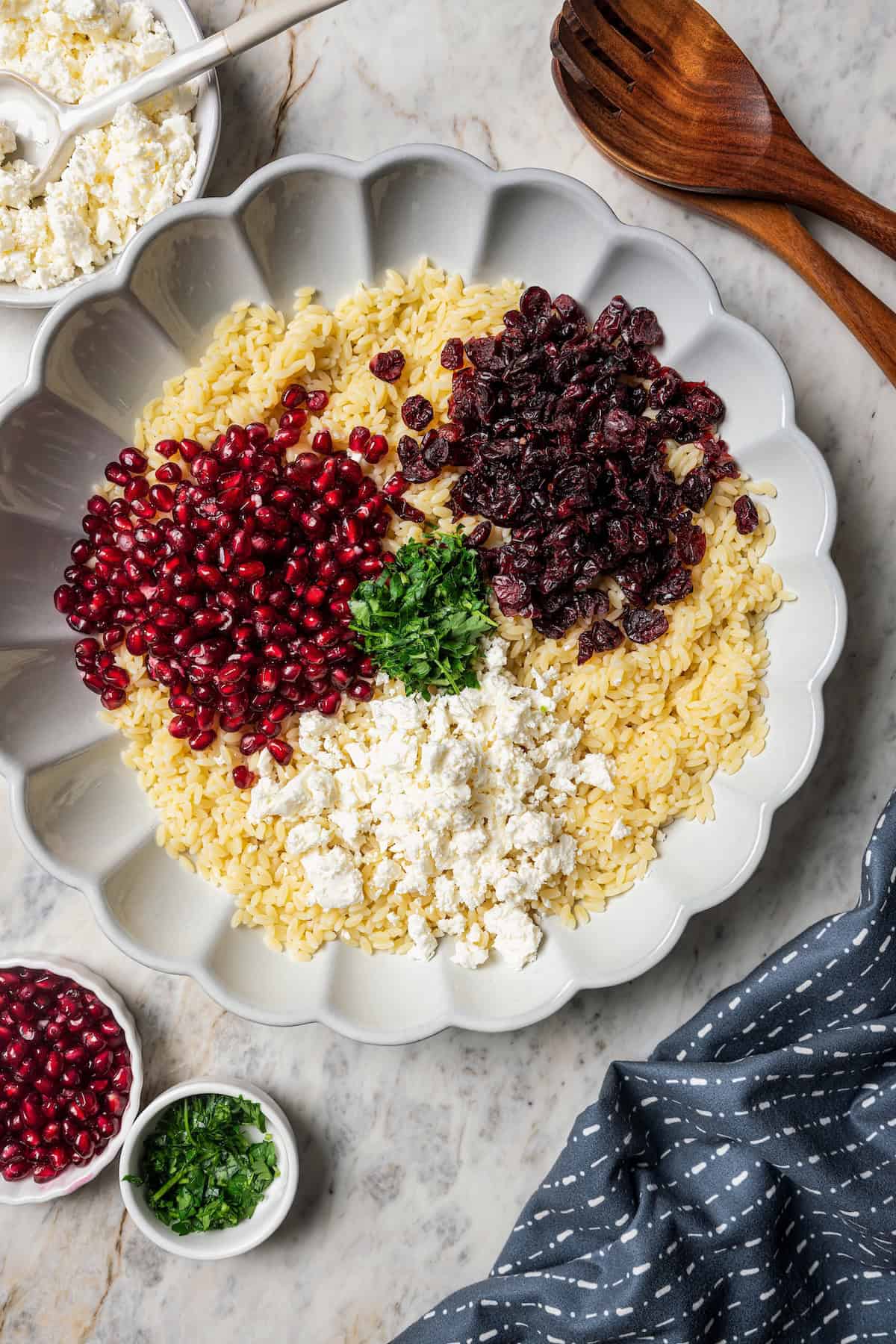 Overhead view of orzo pasta salad ingredients combined in a scalloped bowl.