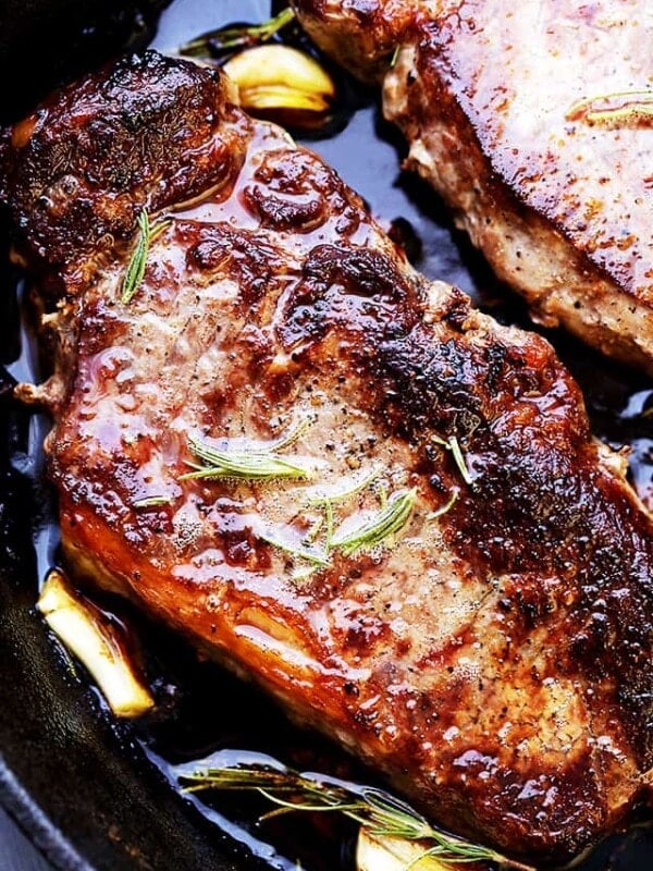 Close up of pan seared steaks in a cast iron skillet with garlic cloves and rosemary.