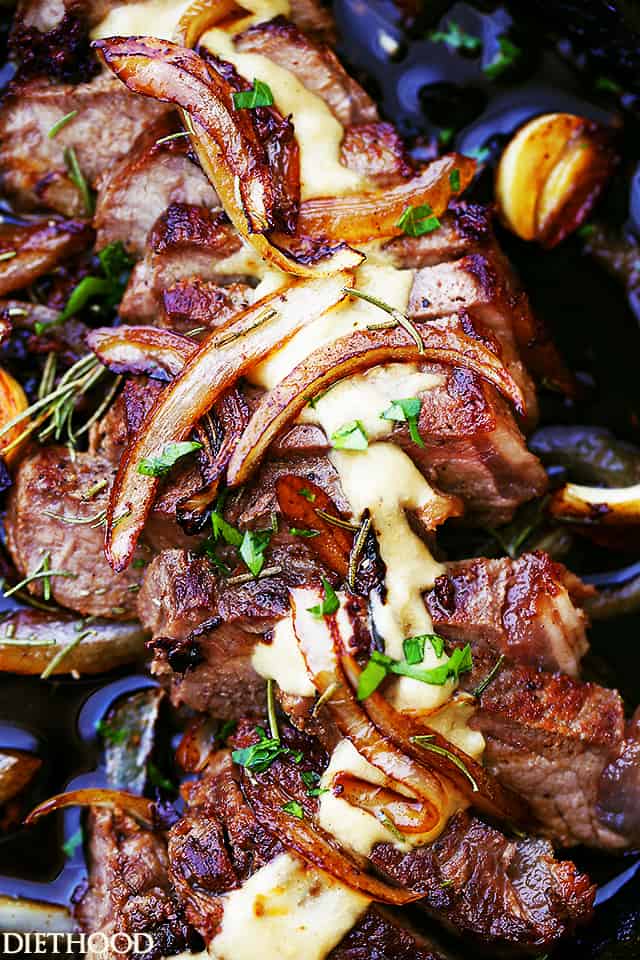 Close up of a sliced pan seared steak in a cast iron skillet topped with caramelized onions and cognac sauce.