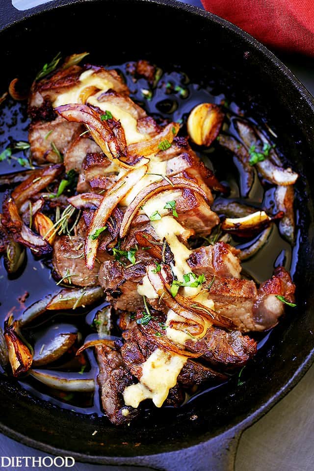 A sliced pan seared steak in a cast iron skillet topped with caramelized onions and cognac sauce.