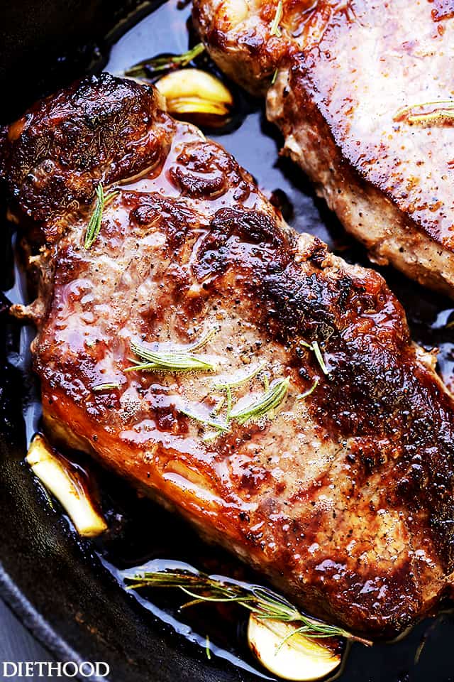 Close up of pan seared steaks in a cast iron skillet with garlic cloves and rosemary.