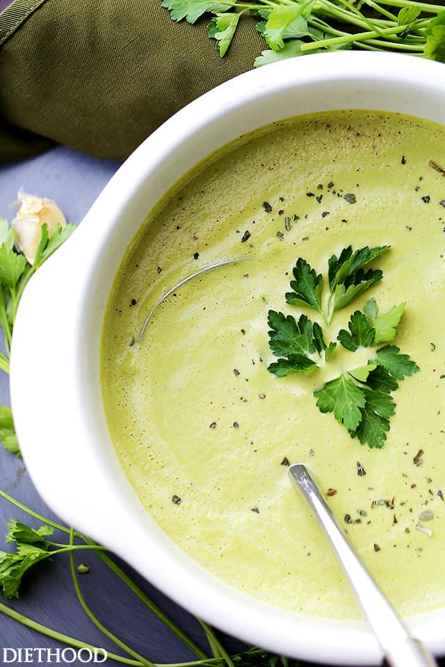 overhead shot of a white pot filled with creamy asparagus soup garnished with fresh parsley.