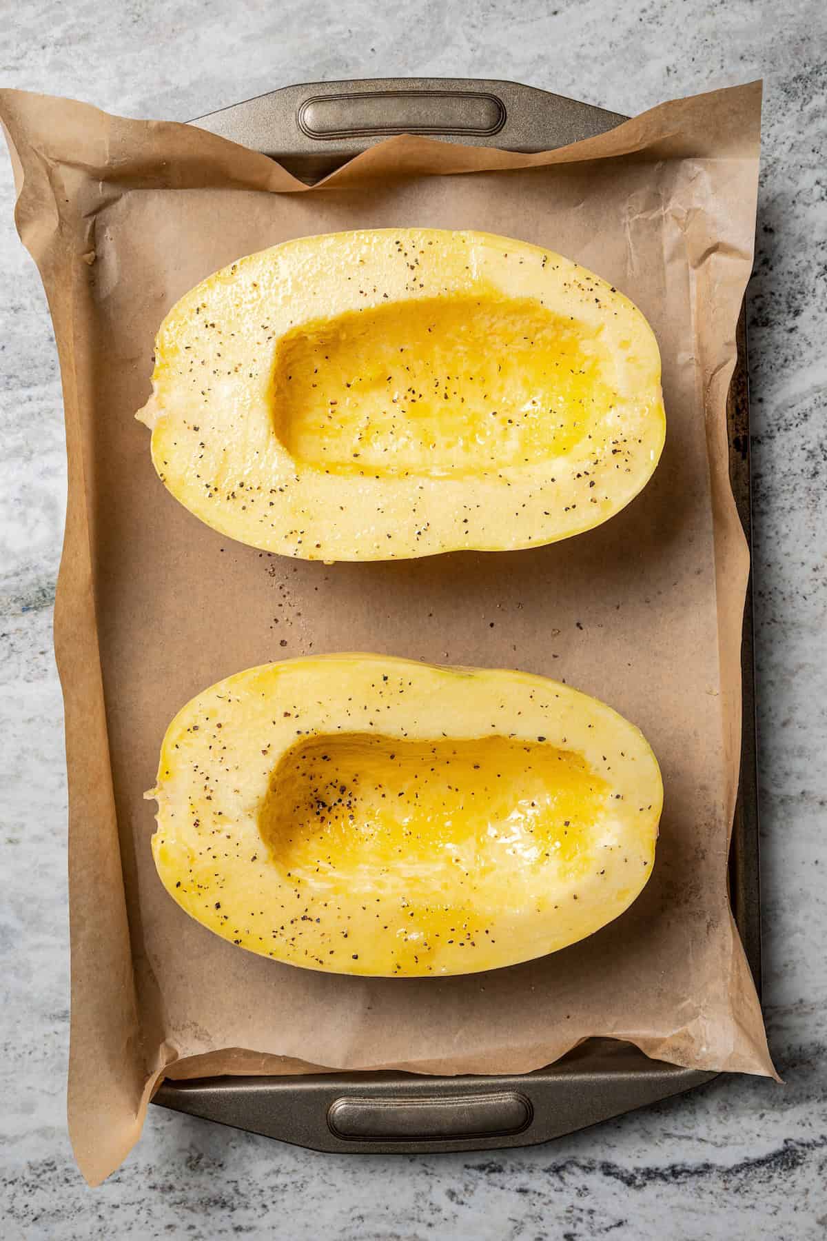 Overhead view of two spaghetti squash halves on a parchment-lined baking sheet.