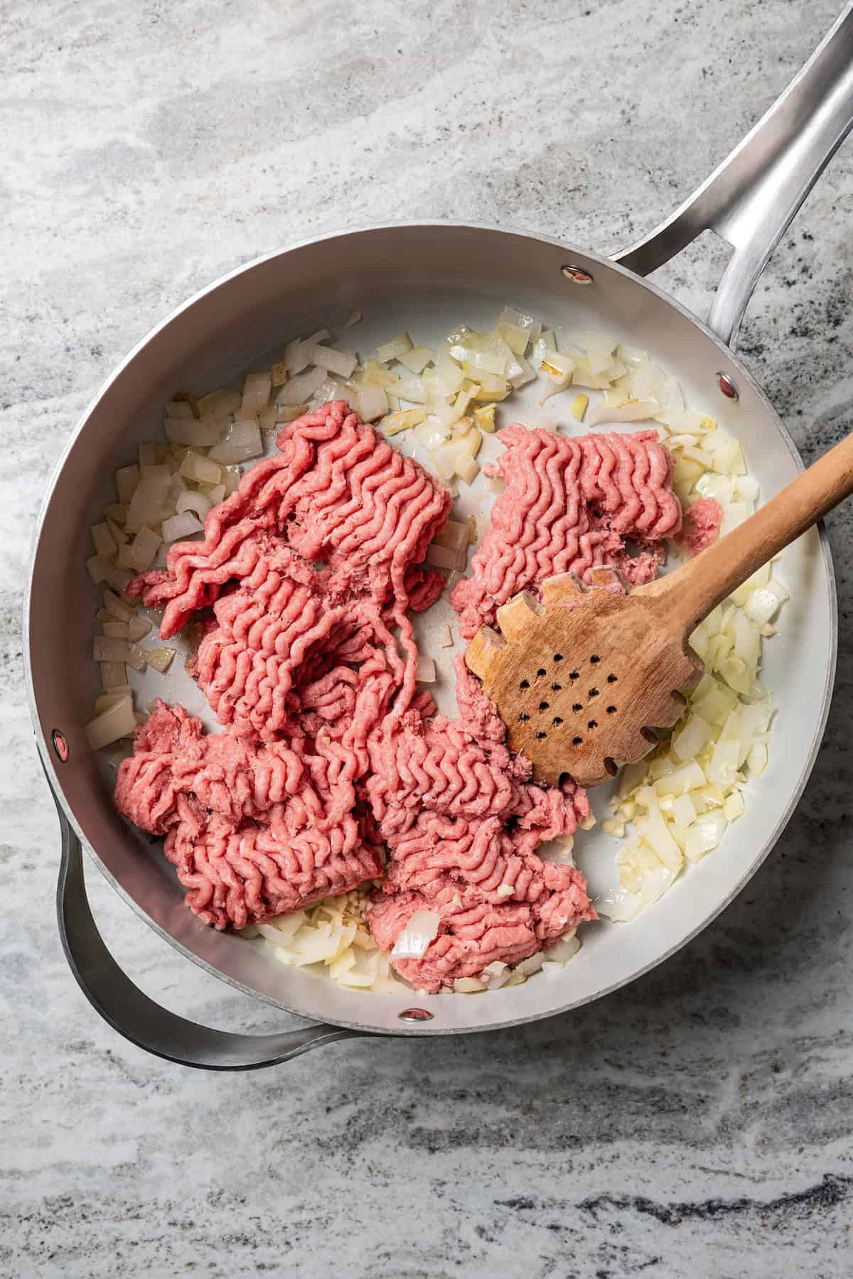 Ground turkey being broken up with a wooden spoon inside a skillet.