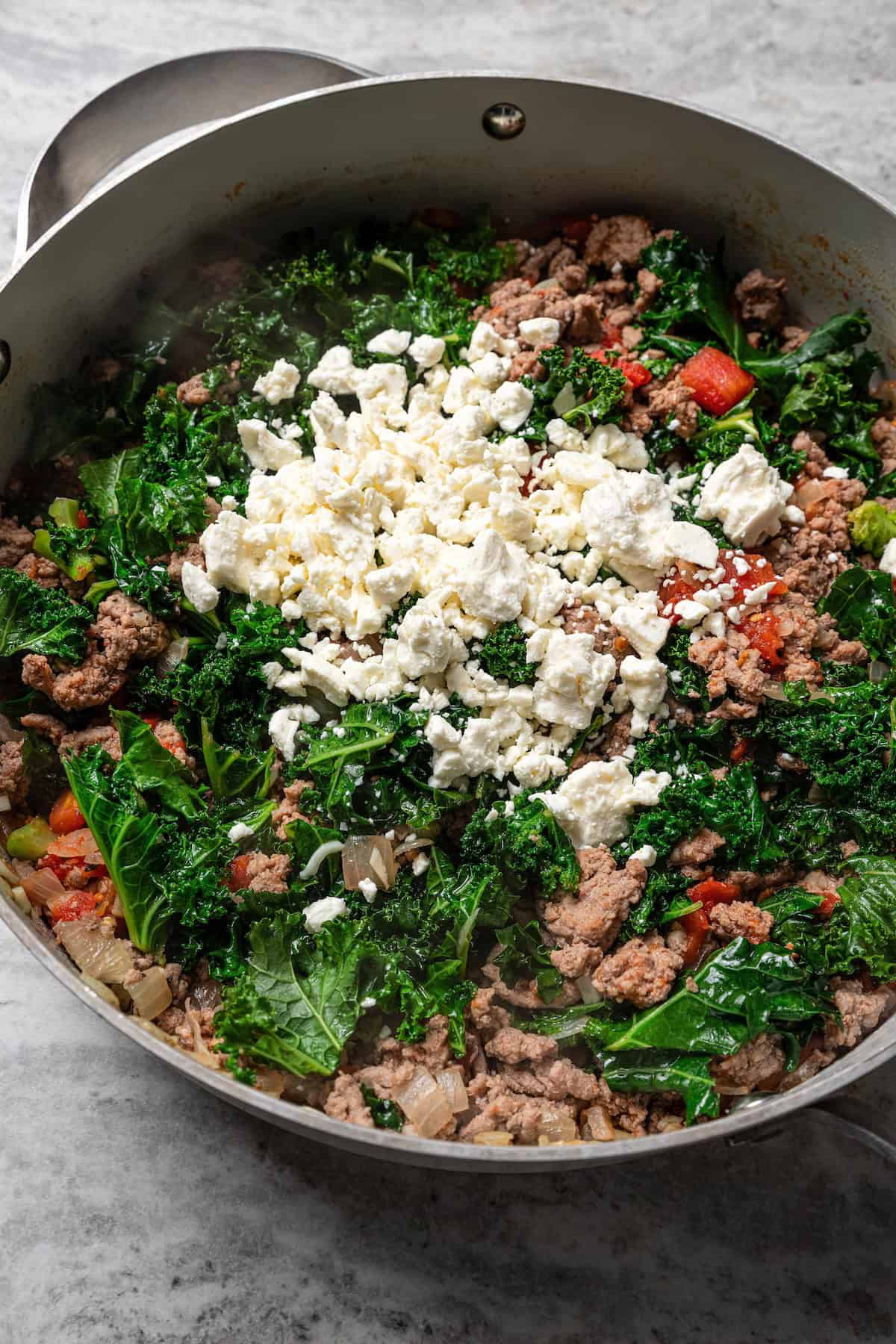 Feta cheese added to the Mediterranean ground turkey filling ingredients in a skillet.