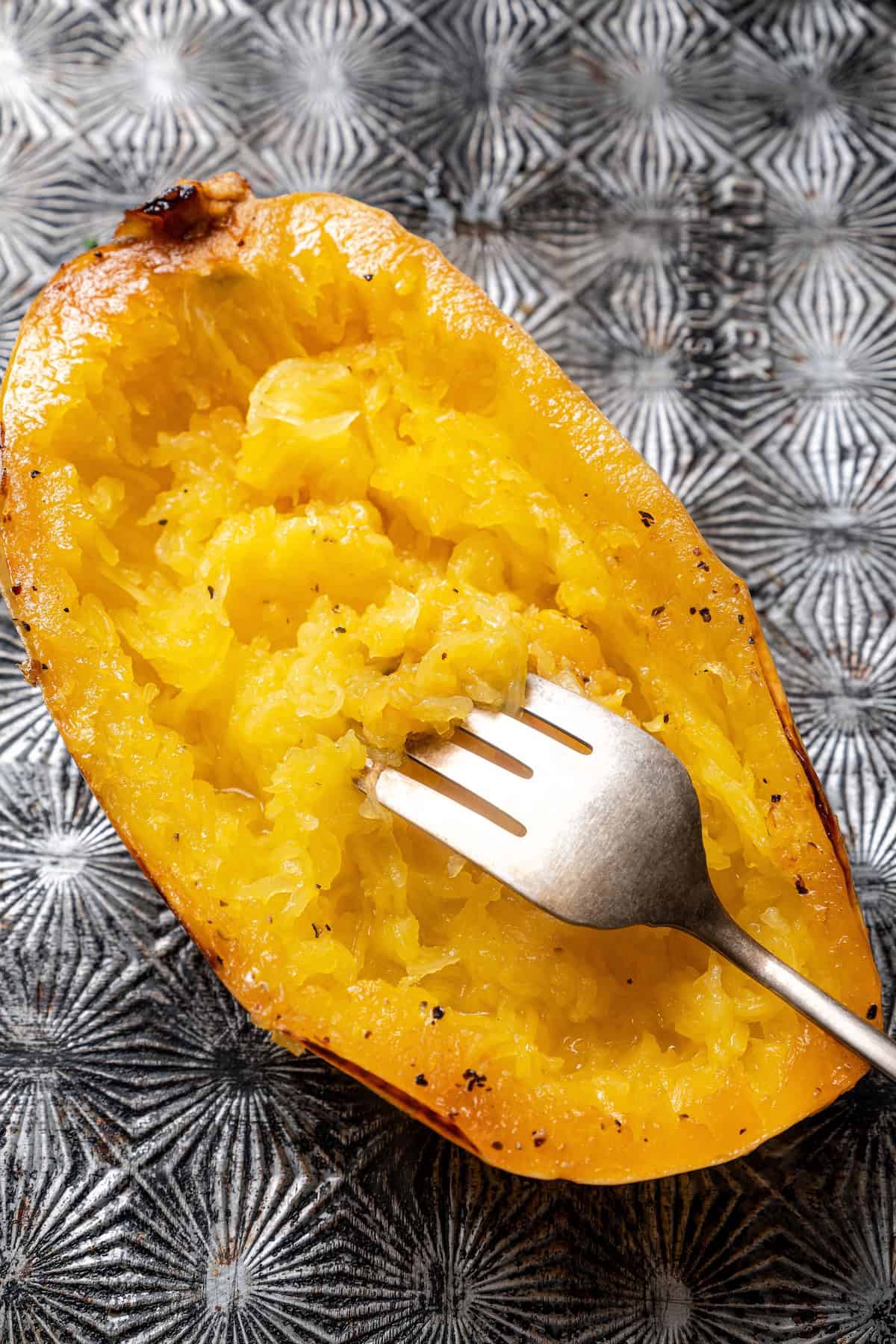 Close up of a fork shredding the flesh inside a spaghetti squash half on a baking sheet.