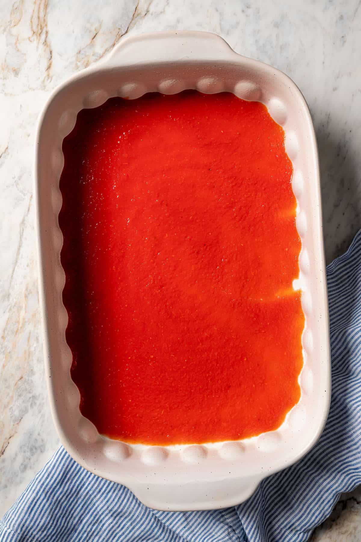 Tomato sauce spread into the bottom of a large casserole dish.