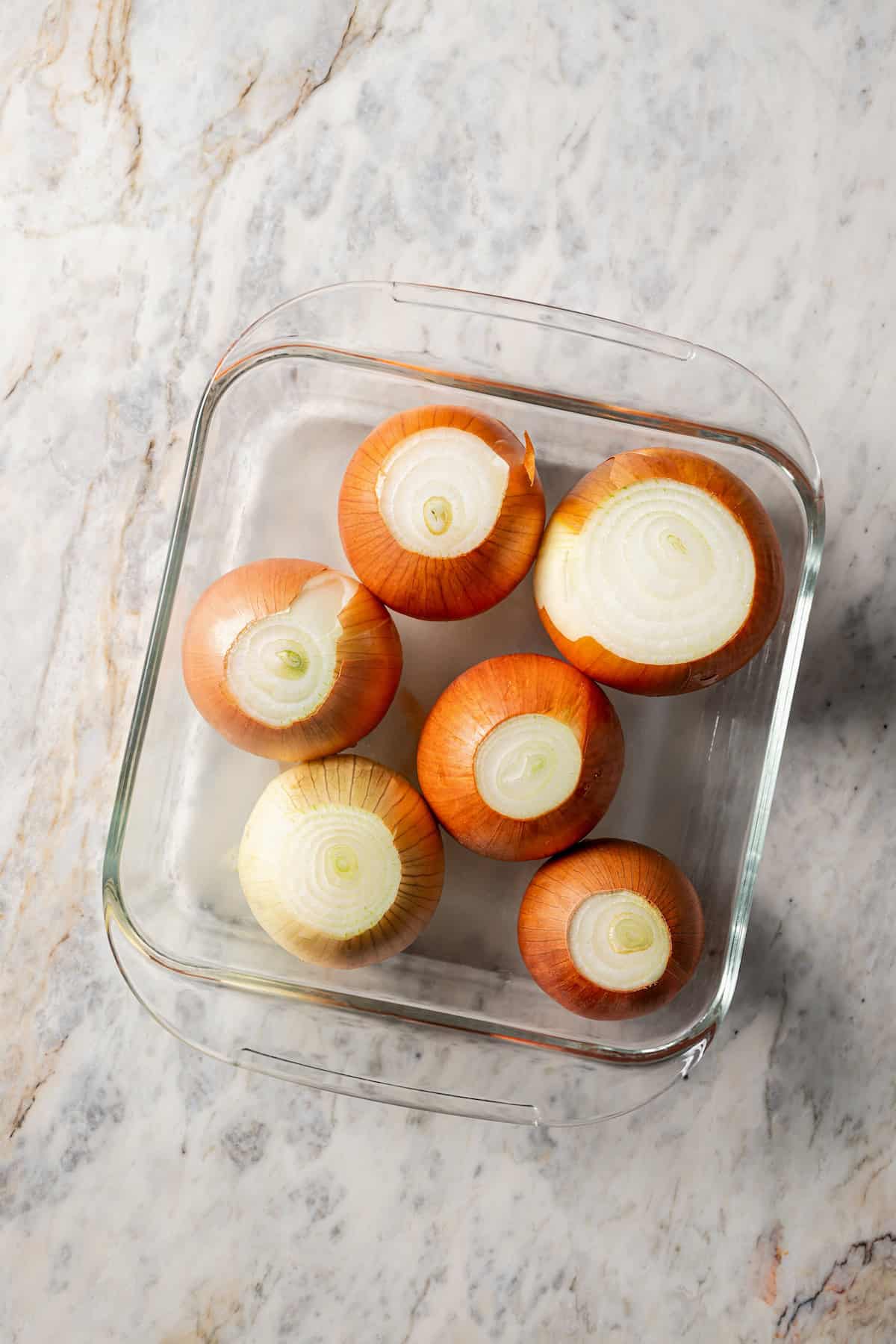 Trimmed onions inside a microwave-safe dish with water.