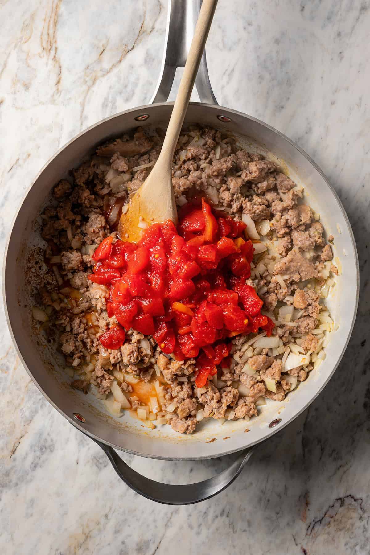 Diced tomatoes added to a skillet with onions and browned Italian sausage.