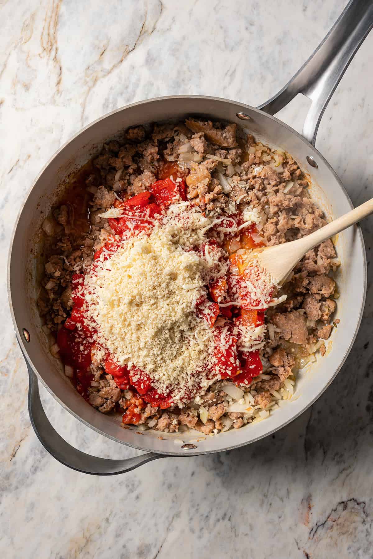 Grated cheese and tomato sauce added to a skillet with browned Italian sausage.