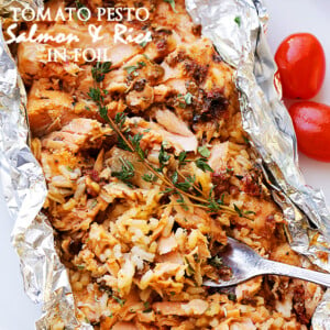 A foil packet that has been torn open to reveal baked salmon with a tomato topping and rice.