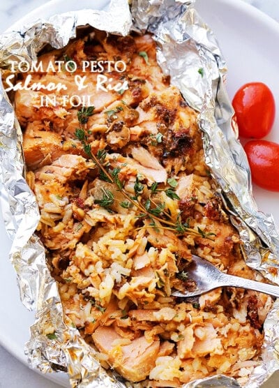 A foil packet that has been torn open to reveal baked salmon with a tomato topping and rice.