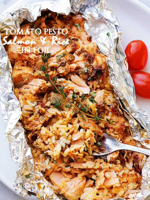A foil packet that has been torn open to reveal baked salmon with a tomato topping and rice.