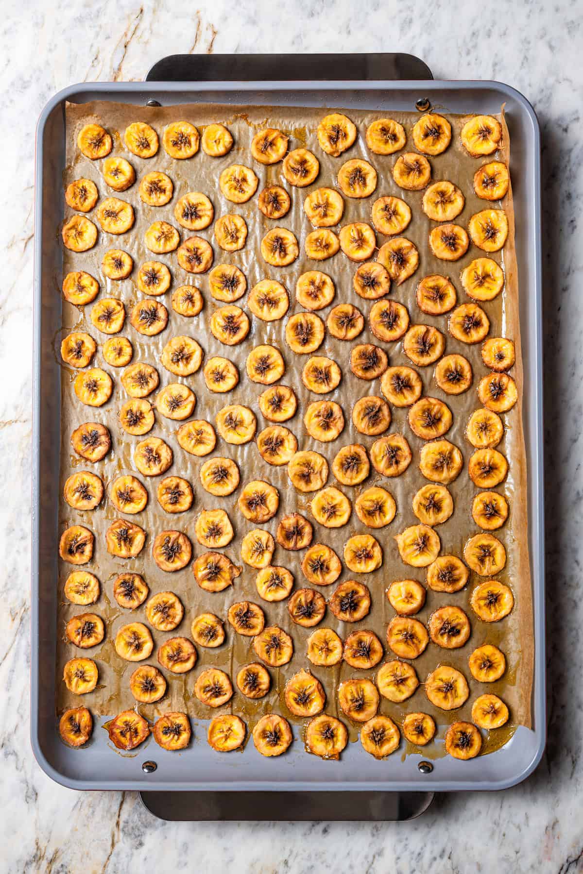 Baked banana chips on a large baking sheet.