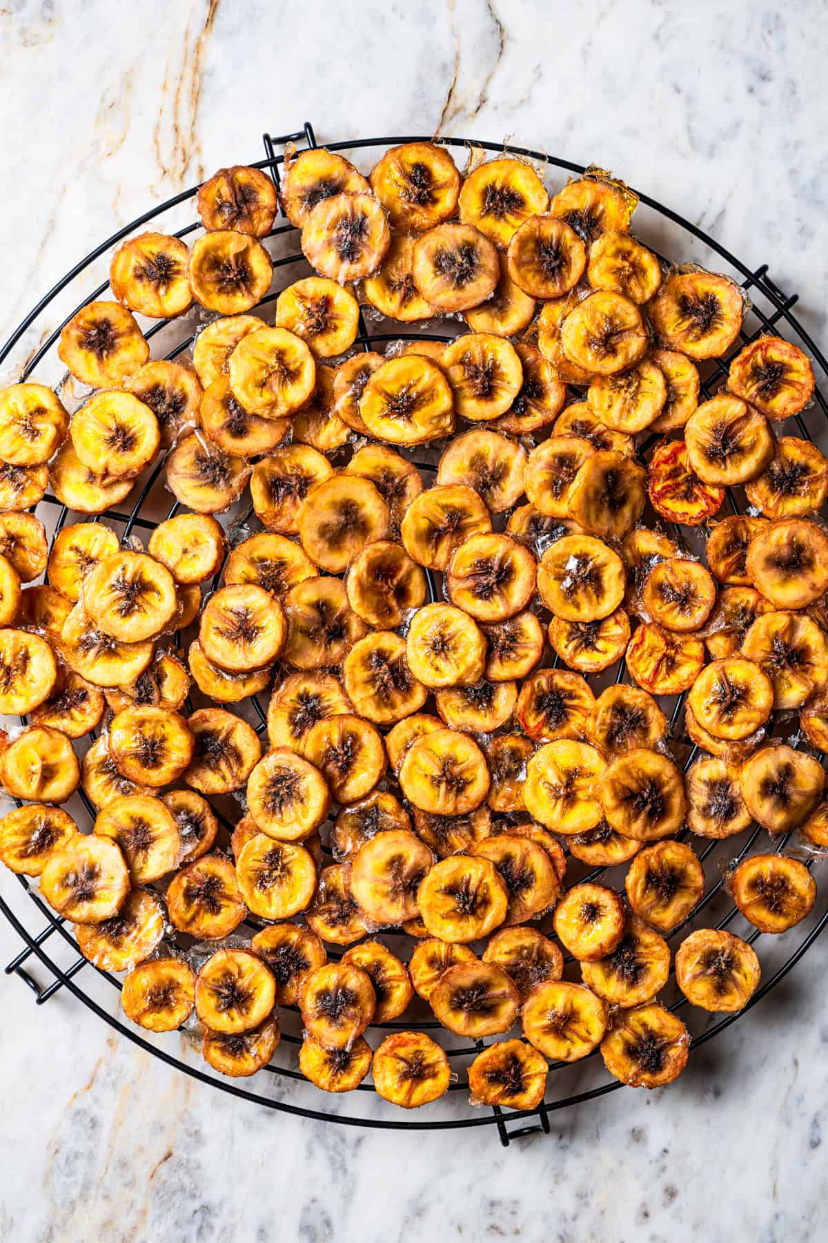 Baked banana chips cooling on a round wire rack.