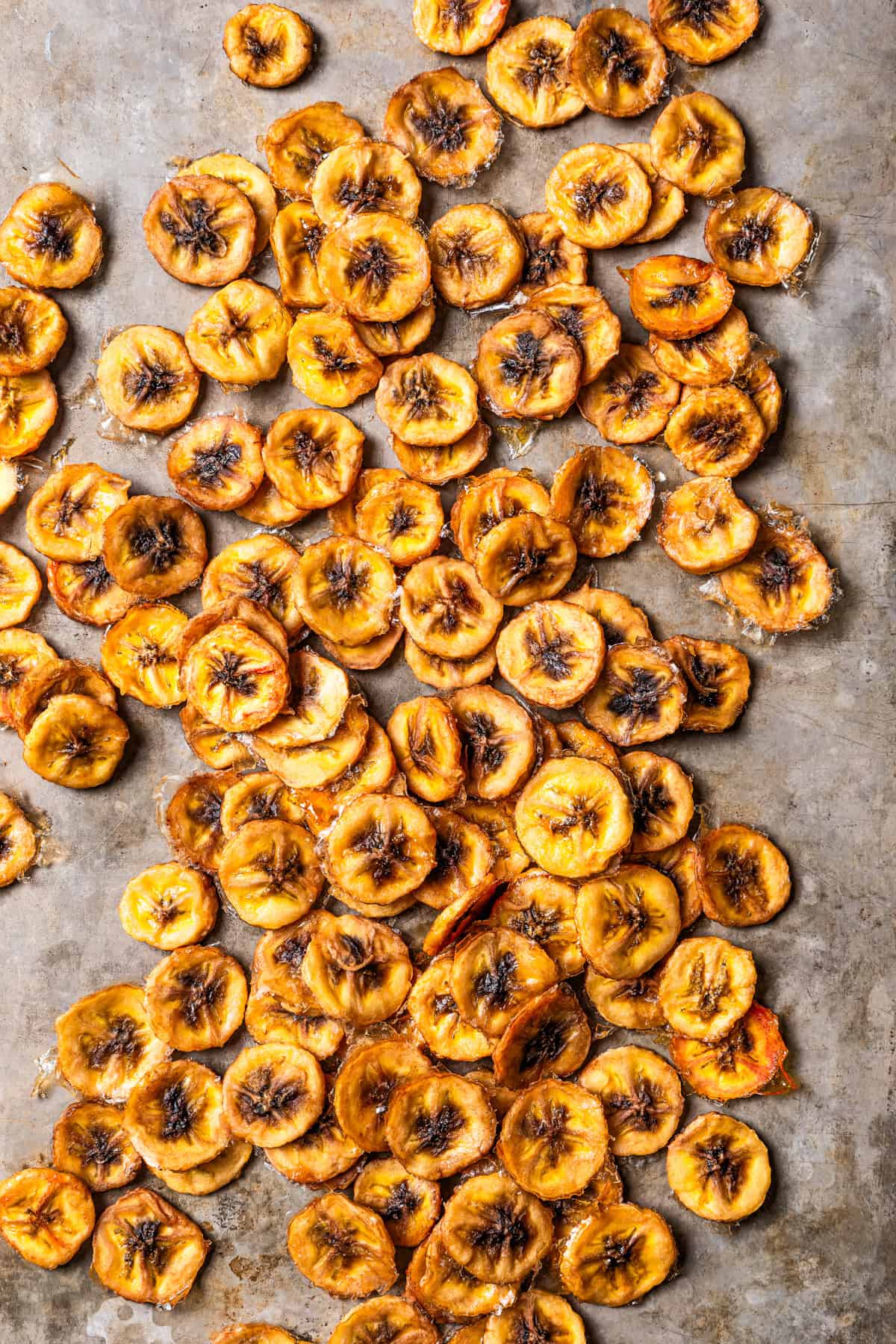 Overhead view of banana chips scattered over a grey surface.