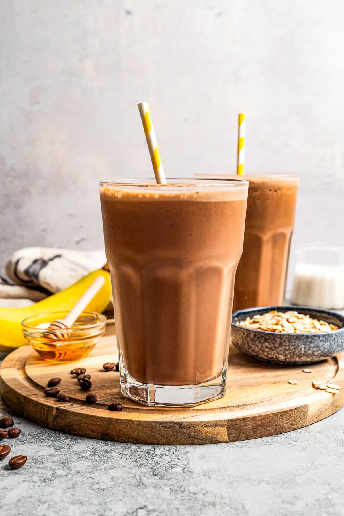 A coffee smoothie in a tall glass with a straw and a second smoothie in the background.