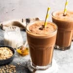 A coffee smoothie in a tall glass with a straw and a second smoothie in the background.