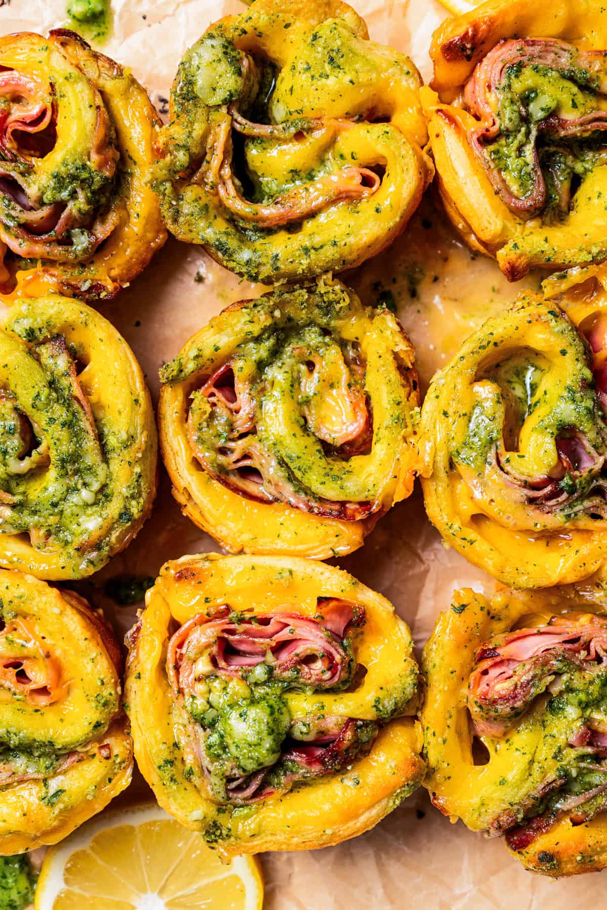 Close up overhead view of baked ham and cheese roll ups on a parchment-lined baking dish.