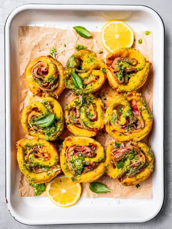 Overhead view of baked ham and cheese roll ups inside a parchment-lined baking pan.