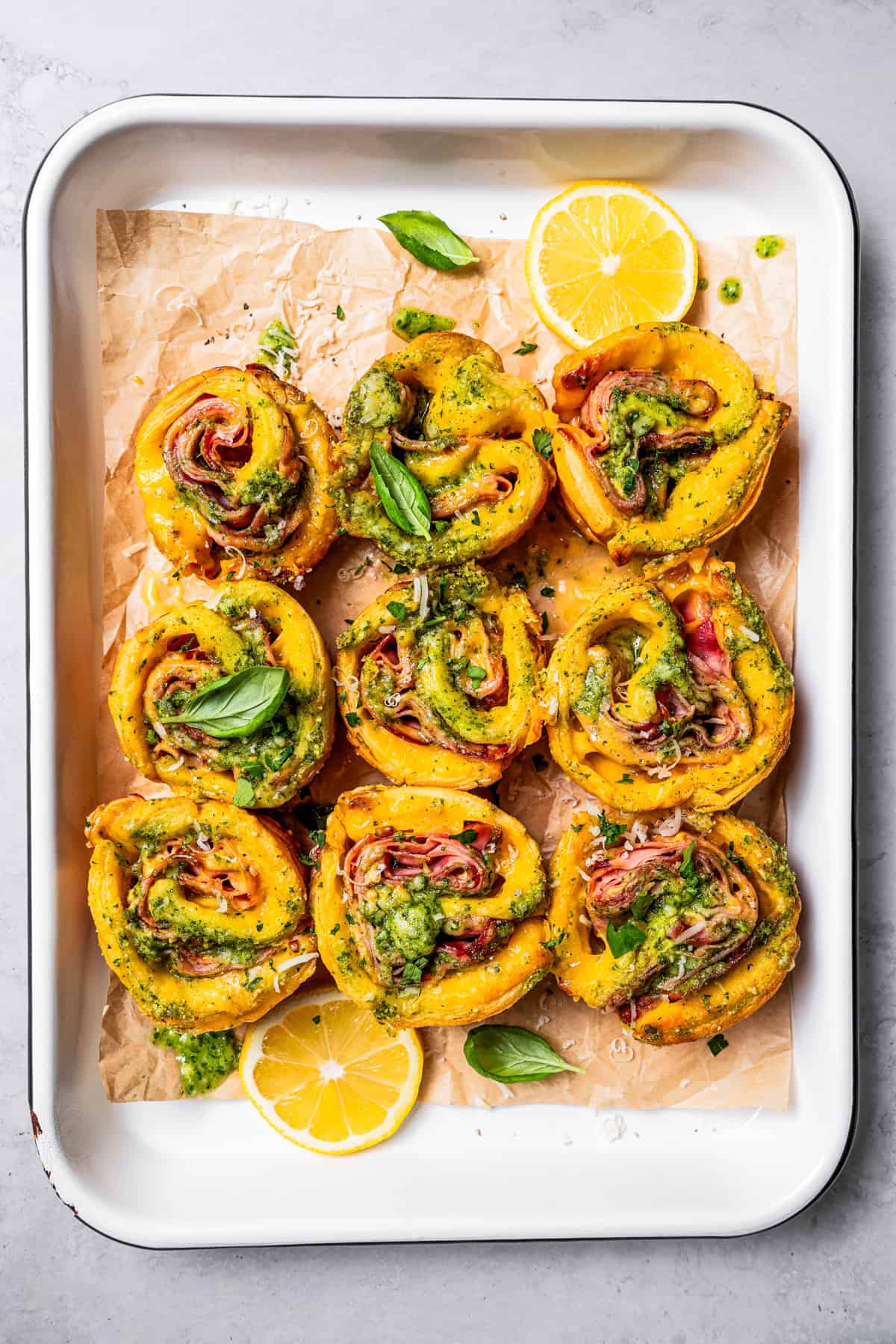 Overhead view of baked ham and cheese roll ups inside a parchment-lined baking pan.