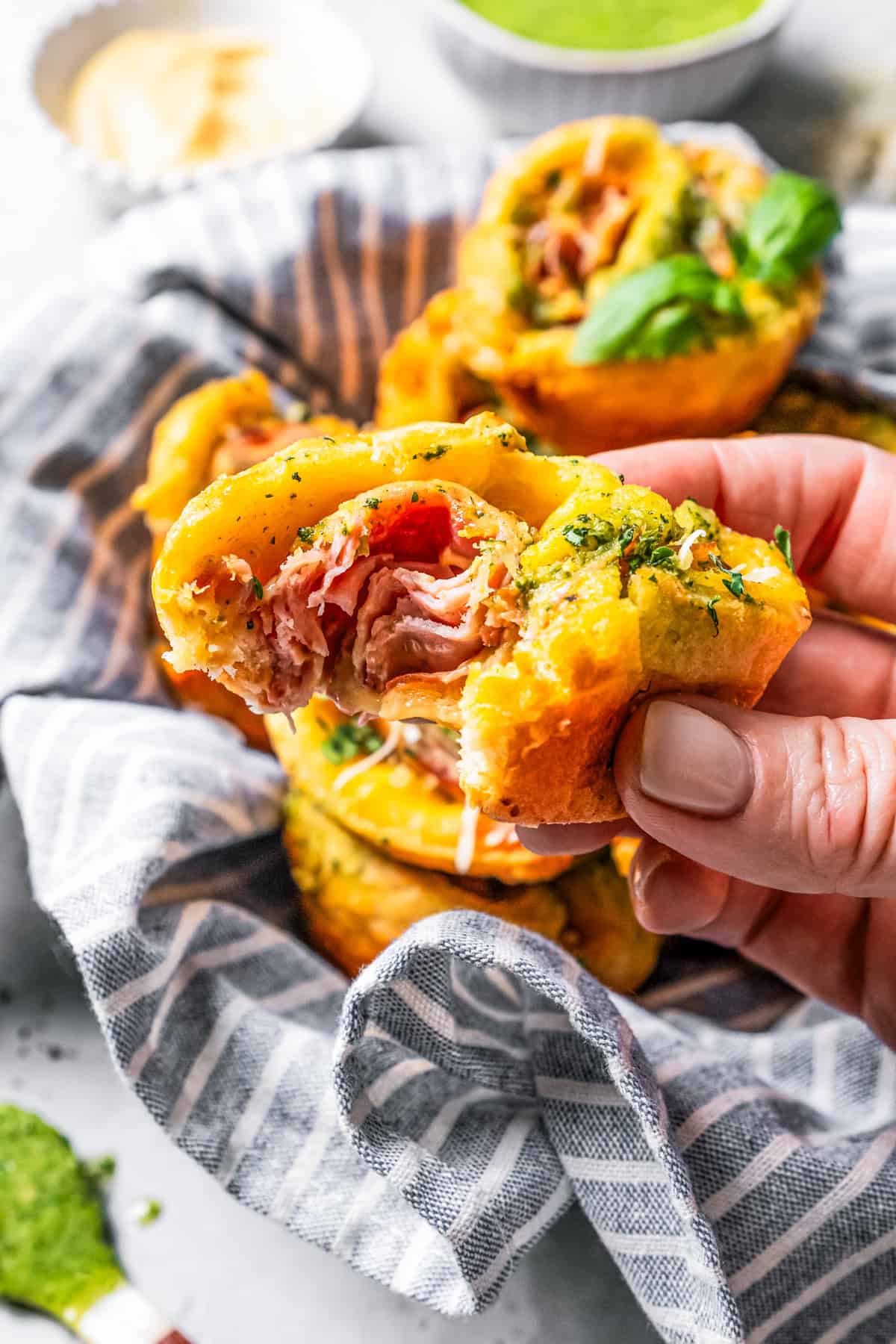 A hand holding up a ham and cheese roll up with a bite missing.