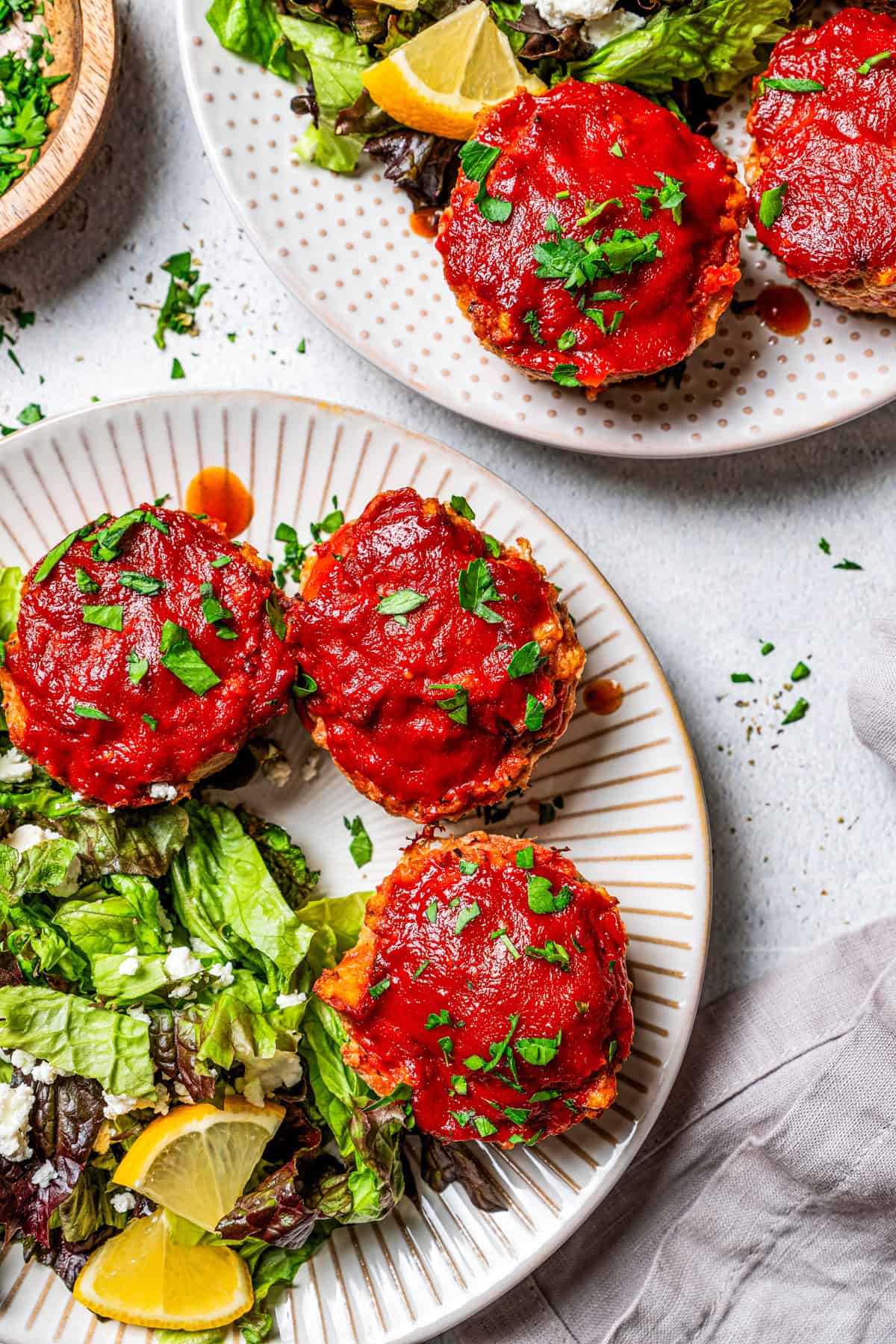 Mini meatloaves served on a plate with a salad, and positioned next to a second plate of mini meatloaves.