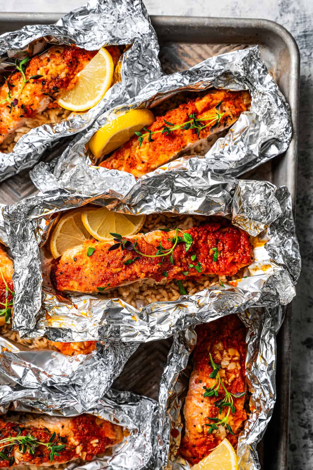 Overhead view of salmon and rice in open foil packets garnished with lemon wedges.