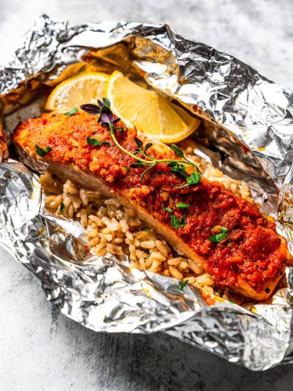 Salmon filet and rice in an open foil packet garnished with lemon wedges.