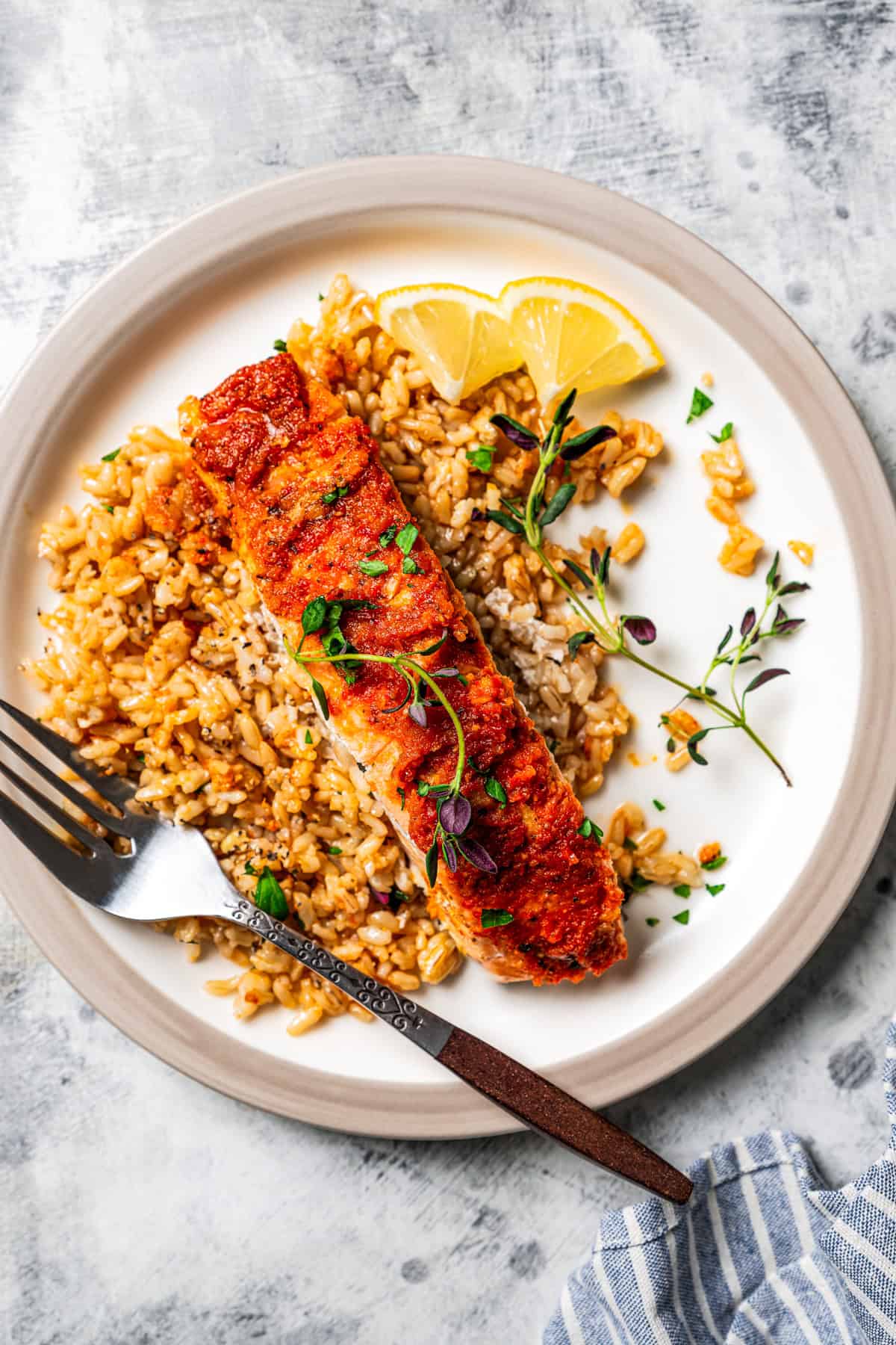 Salmon filet served over a bed of rice on a plate next to a fork and lemon wedges.