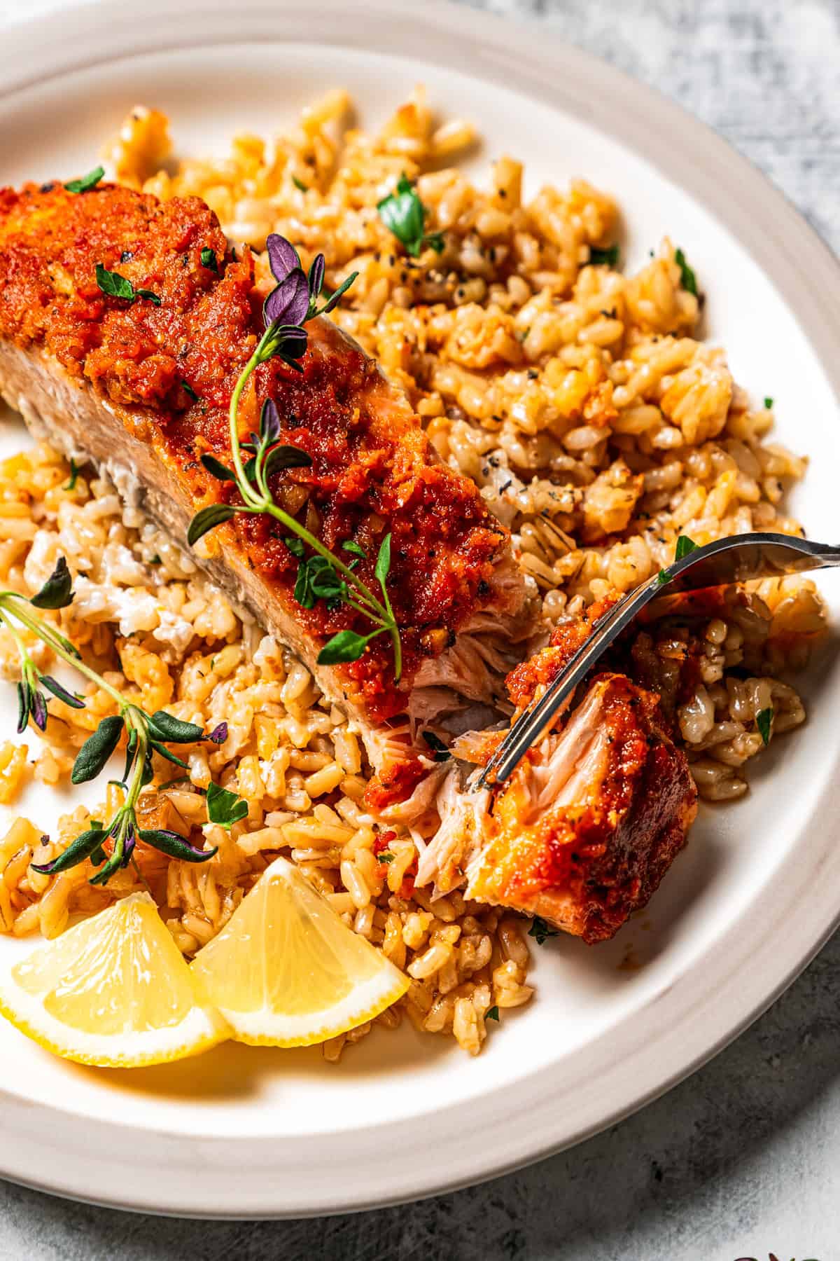 A fork cutting the end from a salmon fillet served over rice.