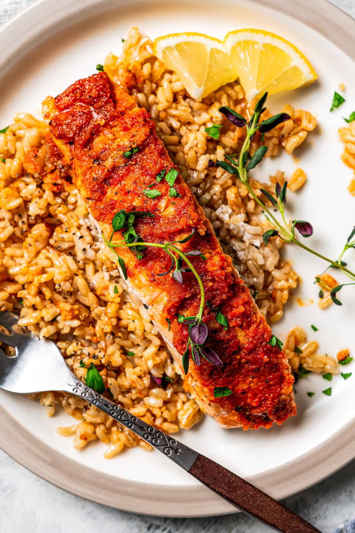 Salmon served over a bed of rice on a plate next to a fork and lemon wedges.